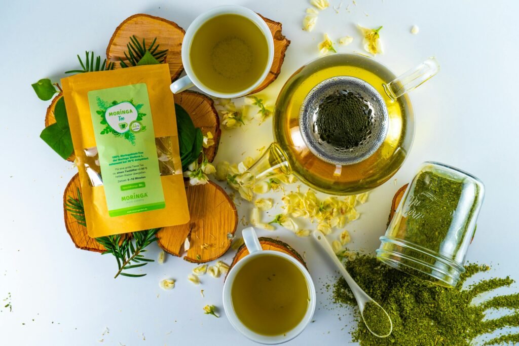 Top-down view of a moringa tea setup with green tea cups, teapot, and moringa leaves.